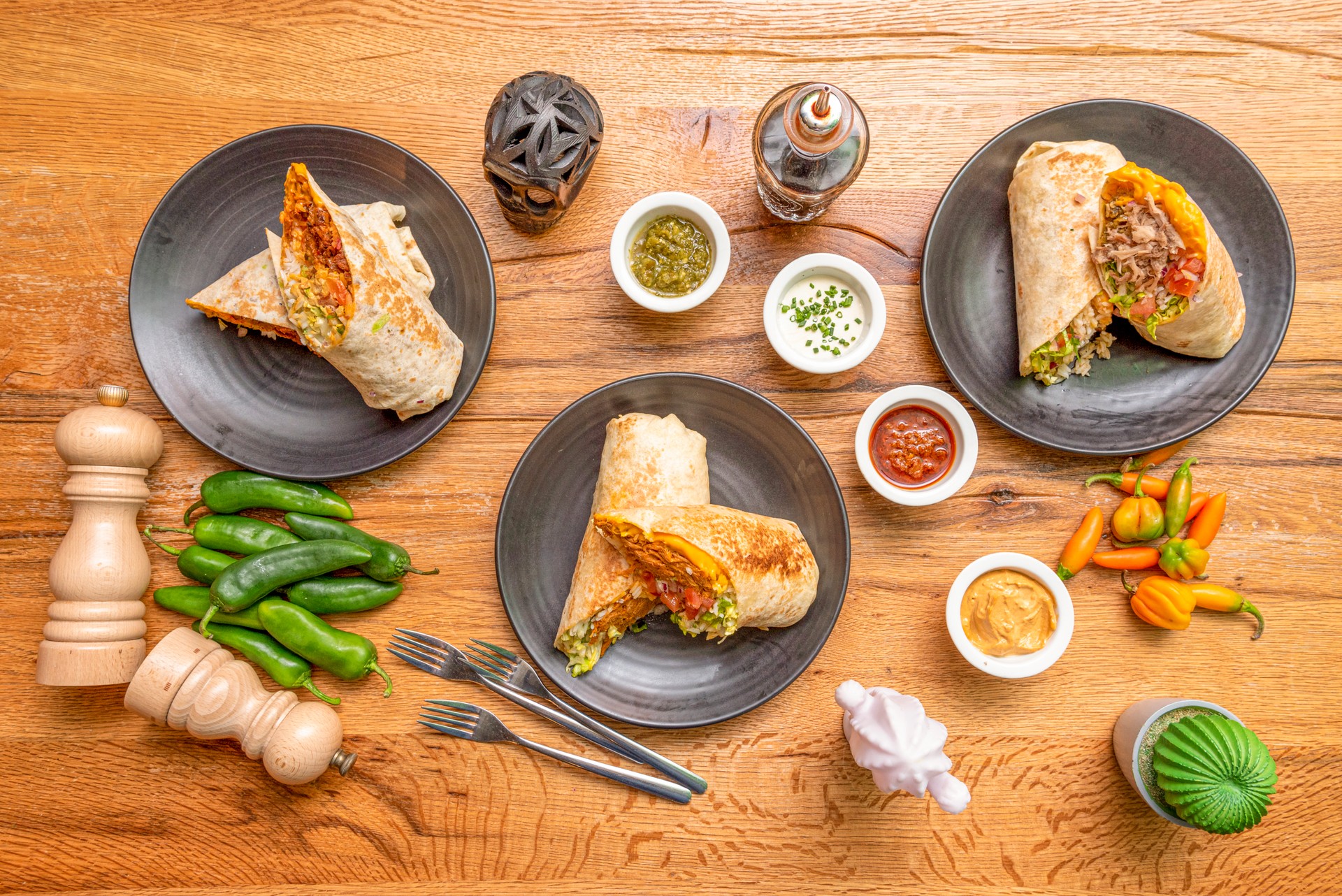 Top view image of Mexican burritos with peppers, sauces, fresh pepper, black skull and forks