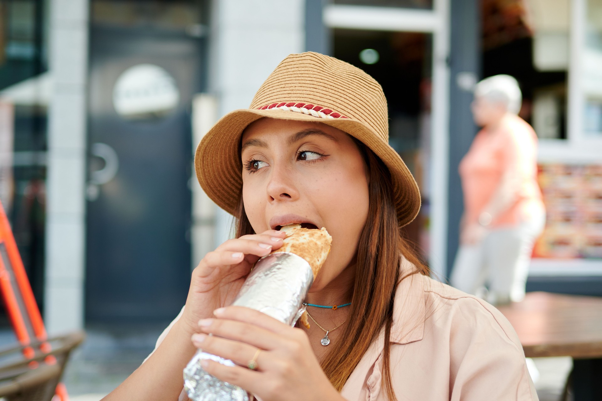 Female in a hat eating a burrito in a street cafe