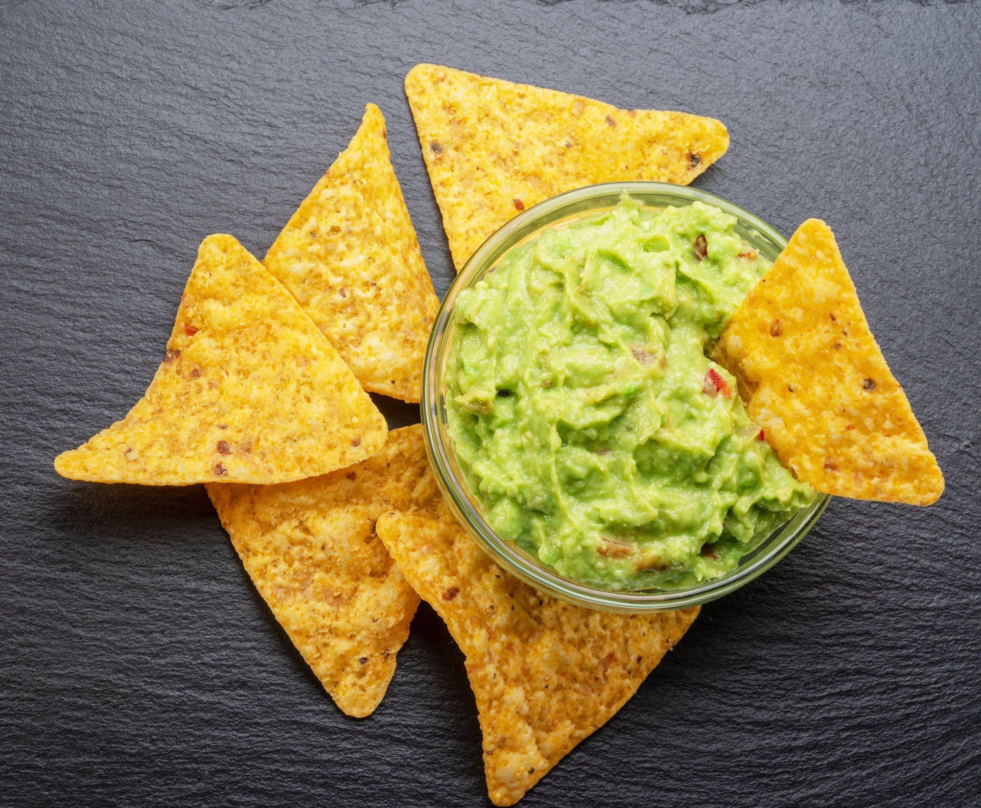 Guacamole sauce and tortilla chips, popular Mexican food, on slate serving board. Top view.